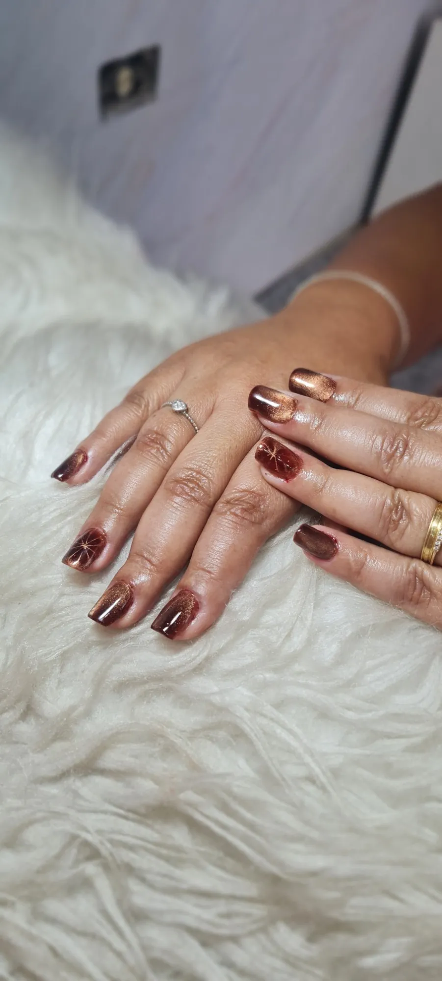 Duas mãos com as unhas blindadas e esmaltadas em tons de cobre